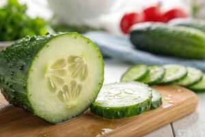 Freshly sliced cucumber on a wooden cutting board with vegetables in the background photo