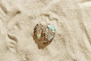 Close-up of colored seashells as heart on textured light beige sand at sunlight, summer and seaside atmosphere, minimal style aesthetic photo, vacation, relaxation, sea, nature love concept photo