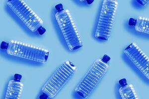 Clear single-use plastic water bottles on light blue background close-up pattern, minimal style aesthetic photo, top view bottled water, Pollution, environmental protection, plastic waste photo