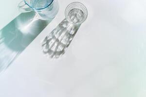 Water Glasses and water jug with Shadows, sunlight Reflection on white background, colored photo minimal style, aesthetic summer still life, refraction throug crystal shine cups, caustics