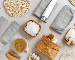 Natural spa, wellness, bath accessory as minimal flat lay pattern, sea salt flakes in wooden bowls, soft gray towels, brush, reusable cotton pads, grey conctrete background, top view neutral colors photo