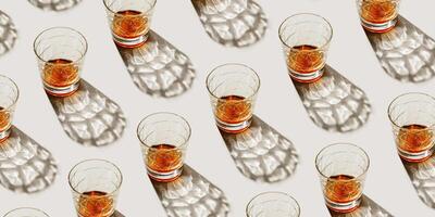 Crystal Whiskey Glasses at sunlight, repeated pattern on beige background, minimal neutral banner, aesthetic top view summer still life, refraction at shine alcohol drink, dark shadow, caustics photo