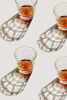 Crystal Whiskey Glasses at sunlight, repeated pattern on beige background, minimal neutral layout, aesthetic top view summer still life, refraction at shine alcohol drink, dark shadow, caustics photo