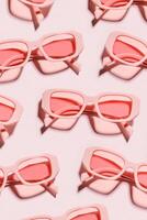 Minimal pattern from pink eyeglasses on rose background, visual trends summer concept. Top view aesthetic photo, colored sunglasses as creative geometric pattern, monochrome flat lay glasses photo