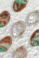 Pattern of abalone seashells floating on clear white water with sun glare and waves. Shells of natural iridescent and rough textures. Minimal aesthetic top view sea ocean life composition, layout photo