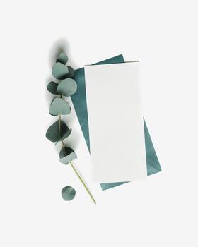 Teal envelope and empty paper card mock up with green eucalyptus on white background. White blank letter on table. Minimal design stationery, flat lay template, top view, copy space. photo