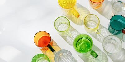 Colorful glowing glass cups on white, casting artistic light reflections and shadows in natural sunlight. Summer drink concept, minimal trend banner, pattern of transparent glasses, caustic effects photo