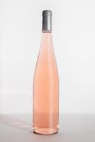 Rose wine bottle on table on white background, side view. Mock up product alcoholic drink, sunlight. One close up bottle Rose wine template, minimal style still life vertical photo, pastel color photo