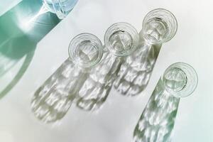 Transparent Water Glasses and water jug with shadows at sunlight on white, pastel color photo minimal style, aesthetic top view shiny cups sparkling at natural light, summer drink, composition.