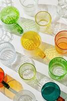 Colorfull glowing glass cups on white background, casting artistic light reflections and shadows in natural sunlight. Summer drink concept, minimal trend pattern of transparent glasses, caustic photo