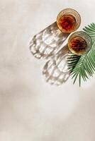 Crystal Whiskey Glasses with shadows at sunlight on beige concrete background, palm leaf decor, minimal aesthetic top view shiny glasses, sun glare, alcohol drink concept, summer still life flat lay photo