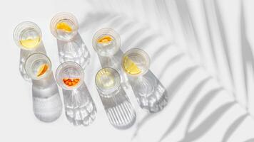 Crystal glasses with citrus slices in water on white background with palm leaf at sunlight, modern, minimal style banner with glass cups with water and citrus fruit, as lemon, orange photo
