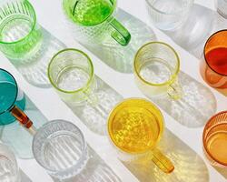 Colored shiny drink Glasses still life with shadow and sunlight reflections on white, minimal aesthetic top view summer photo, refraction at glass cups with sun flare, creative modern pattern photo