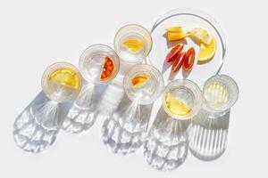 Citrus Infused Water in clear Glasses and plate, artistic light reflections and shadow in natural sunlight. Summer drink concept, minimal pattern, flavored water with yellow red slices of fruit photo