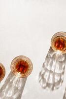 Whiskey Glasses with Shadows and sunlight Reflection on beige background, minimal aesthetic top view summer still life, refraction throug crystal shine cups, caustics effect, vertical photo