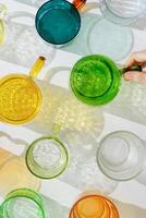 Colored glowing glass cups on white background, casting artistic light reflections and shadows in natural sunlight. Summer drink concept, minimal trend pattern of transparent glasses, caustic photo