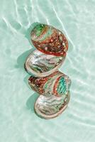 Abalone seashells floating on clear turquoise water with sun glare and waves. Shells of natural iridescent and rough textures. Minimal style top view pattern sea and ocean life background photo