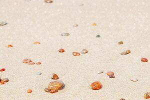 Sea stones amber yellow colored on natural fine beige sand shore background, copy space. Natural colorful pebbles, monochrome Minimal nature summer landscape, beautiful beach, soft focus photo