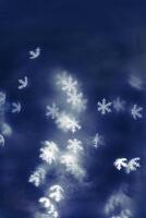 White snowflakes bokeh lights on blue background, abstract winter holiday wallpaper with optical blurred glittering pattern. Christmas or New Year abstract composition as backdrop, monochrome photo