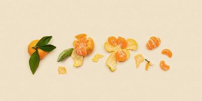 Set of fresh orange yellow tangerines with green leaves, whole and pieces on beige background, minimal style flat lay. Citrus fruits mandarines as still life aesthetic banner, top view pattern photo