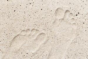 Woman footprint close up on sand on seashore. Imprint female bare feet on white beige sand. Summer rest or vacation on beach concept. Top view natural sandy texture with footsteps photo