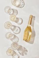 Summer party drinks flat lay, wine glasses with white sparkling wine and sunshine shadow on light table. Minimal pattern with beautiful wine glasses, above view still life, beige golden colored photo