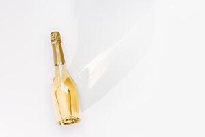 Top view white sparkling wine bottle with sunshine long shadow and flare on light white background. Minimal aesthetic flat lay, one champagne bottle with golden. Summer alcohol drink photo