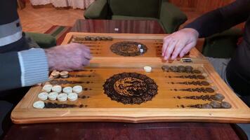 Grandpa throws dice on wooden board and makes move in backgammon. Complex strategic board game. Choosing the right move in backgammon to win the board game, seniors play games video