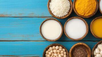 Bowls of plant based milk soy beans coconut turmeric and spices on blue wooden background Healthy vegan food concept photo
