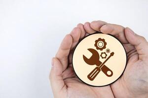 Hand holding paper with gear icon and mechanic tools. Concept of maintenance, process of maintaining and repairing equipment or systems to work efficiently. photo