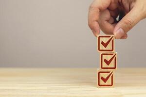 Hand picks up a stack of wooden blocks with check icons. checklist survey concept, and evaluation Accreditation, quality assurance. with copy space and business design. photo