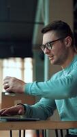 Man working on laptop and drinking coffee from a paper cup. Positive smiling businessman typing on computer sitting in comfortable office. Vertical video