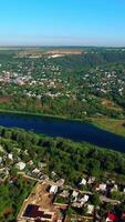 Dark blue river dividing the city into two parts. Dense architecture mixed with the beautiful greenery at backdrop of blue clear sky. Top view. Vertical video