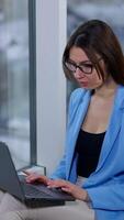 Freelancing woman working on laptop holding it on laps. Lady is puzzled with some problem occurred on computer. Vertical video
