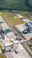 Modern agrocomplex on field. Grain elevators for storing crop. Large industrial territory with storage tanks. Freight trains on rails. Aerial view. Vertical video