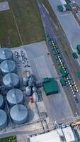 Steel granary storage tanks on field. Flight over modern agriculture complex with silver silos for storing crop. Top view. Vertical video