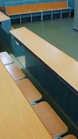 Empty auditorium for students. Rows of wooden tables and chairs in the university. Nobody in the class during pandemic. Vertical video