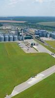 Panoramic view of a modern factory on green nature background. Grain elevators on field. Large agriculture complex among environment in summer. Aerial view. Vertical video
