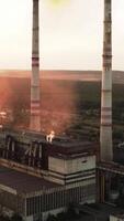 Dangerous manufacture with smoke at sunset. Industrial plant pollutes the air in the evening. Large chimneys of factory. Pollution the atmosphere. Aerial view. Vertical video