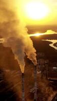 Top view on two pipes with smoke. Factory on the natural fields background at sunset. Pollution the air. Aerial view. Vertical video