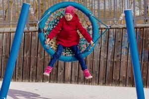 Caucasian smiling child of 8 9 years swinging on round seesaw looking at camera in motion photo