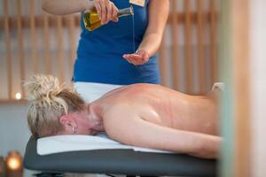 A professional massage therapist pours aromatic oil into their hands, preparing for a relaxing and rejuvenating massage session in a serene spa setting. photo