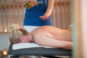 A professional massage therapist pours aromatic oil into their hands, preparing for a relaxing and rejuvenating massage session in a serene spa setting. photo
