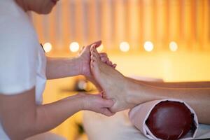 Foot Massage Therapy in a Relaxing Spa Setting. A professional massage therapist in a white uniform provides a soothing foot massage to a client in a calm and serene spa environment photo