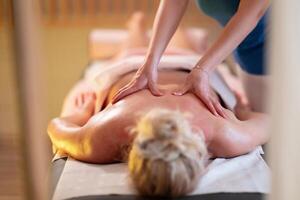 Relaxing Back Massage in a Spa Setting. A professional massage therapist in a blue uniform provides a relaxing back massage to a client lying on a massage table. photo