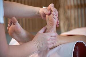 Foot Massage Therapy in a Relaxing Spa Setting. A professional massage therapist in a white uniform provides a soothing foot massage to a client in a calm and serene spa environment photo