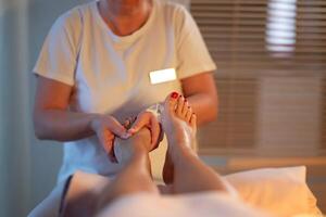 Foot Massage Therapy in a Relaxing Spa Setting. A professional massage therapist in a white uniform provides a soothing foot massage to a client in a calm and serene spa environment photo