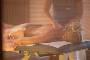 Relaxing Back Massage in a Spa Setting. A professional massage therapist in a blue uniform provides a relaxing back massage to a client lying on a massage table. photo
