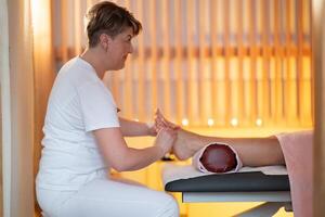 Foot Massage Therapy in a Relaxing Spa Setting. A professional massage therapist in a white uniform provides a soothing foot massage to a client in a calm and serene spa environment photo