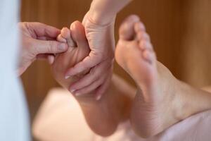 Foot Massage Therapy in a Relaxing Spa Setting. A professional massage therapist in a white uniform provides a soothing foot massage to a client in a calm and serene spa environment photo